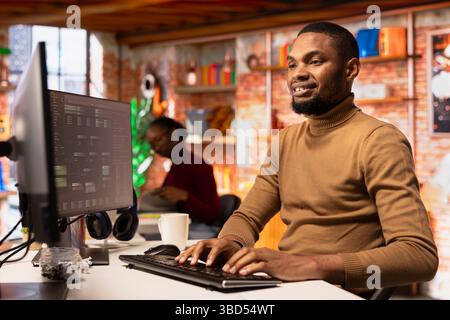 Upbeat IT engineer coding advanced AI algorithm in startup office, refining machine learning models to enhance automation. Cheerful man using coding platform in Silicon Valley workplace Stock Photo