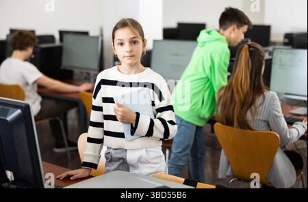Teen schoolgirl with workbook in hands standing in computer class Stock Photo