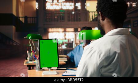 Young man medical student does research for exams next to chroma key, reviewing pharmacology papers under a green lamp. Focusing on exam preparations and their career in medicine. Camera A. Stock Photo