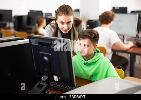 Female teacher consulting tween boy studying in computer class Stock Photo