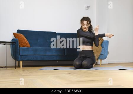 Young woman warming up arm muscles before doing fitness exercises at home Stock Photo