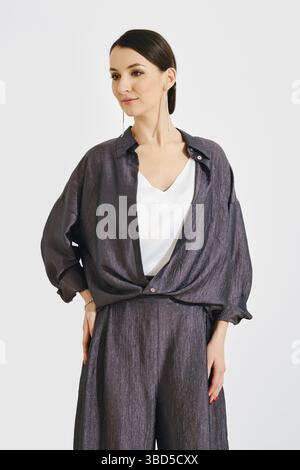 A young woman stands with a confident posture, dressed in a sleek, modern outfit featuring a relaxed top and trousers. Her expression is calm, highlig Stock Photo