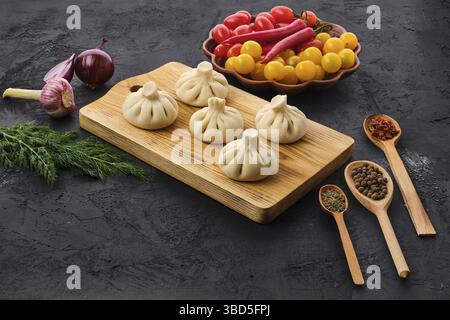 Uncooked khinkali on black wooden board with spice and herbs Stock Photo