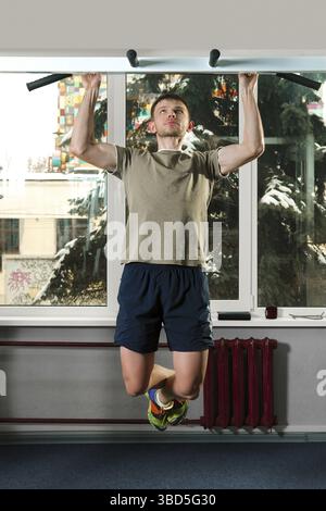 Athletic man pulling up in gym with crossed legs. Fitness workout Stock Photo