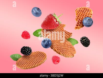 Tasty Dutch waffles, fresh berries and mint flying on pink gradient background Stock Photo