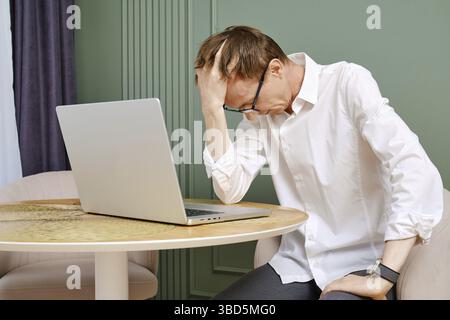 Upset and tired middle aged man with laptop lower his head Stock Photo