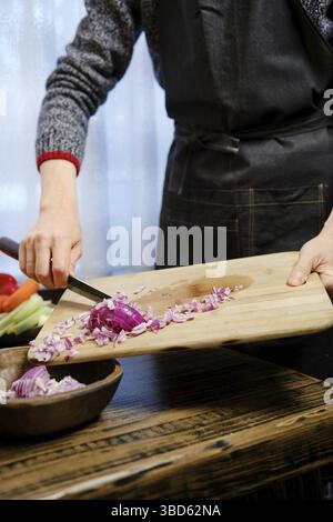 Unrecognizable man puts chopped red onions from a wooden cutting board in wooden bowl in the kitchen Stock Photo