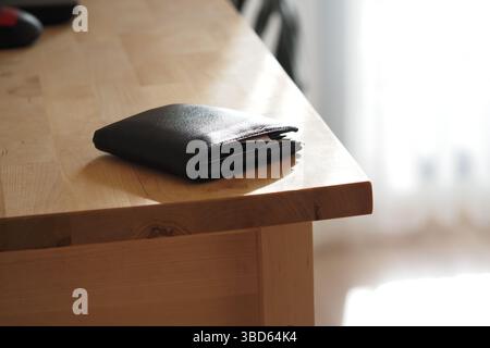 Black wallet resting on wooden table in bright room Stock Photo