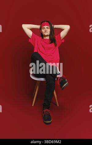 Man threw his hands behind his head and sits relaxed on chair in red studio Stock Photo