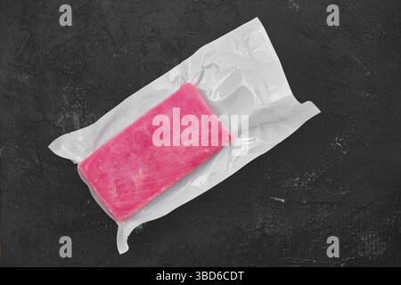 Raw frozen tuna fillet in vacuum packaging on black background Stock Photo