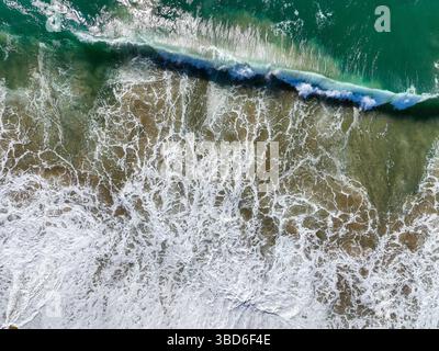Drone photo showing ocean waves hitting a beach and forming foamy textures Stock Photo