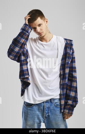 Young cocky man in checkered shirt and jeans touching his head Stock Photo