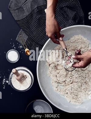 Person stretches dough on a dark surface dusted with flour. Stock Photo
