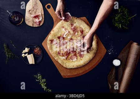 Person stretches dough on a dark surface dusted with flour. Stock Photo