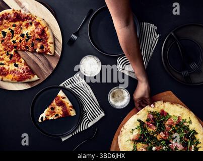 Person stretches dough on a dark surface dusted with flour. Stock Photo