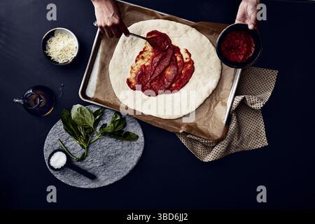 Person stretches dough on a dark surface dusted with flour. Stock Photo