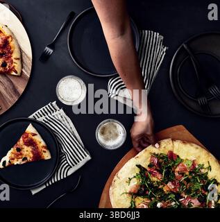 Person stretches dough on a dark surface dusted with flour. Stock Photo