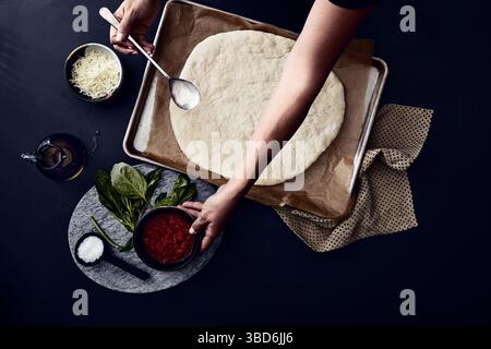 Person stretches dough on a dark surface dusted with flour. Stock Photo