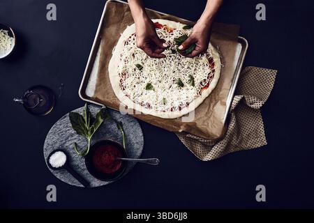 Person stretches dough on a dark surface dusted with flour. Stock Photo