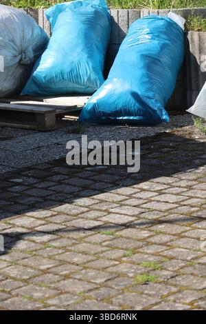 A pile of blue plastic bags sit on a brick walkway Stock Photo