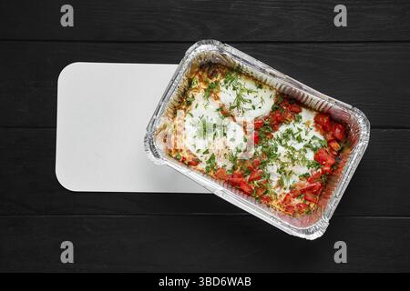 Overhead view of eggs fried with ham and tomato in take away foil package Stock Photo