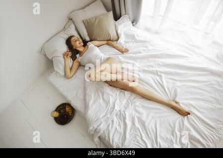 Lazy weekend morning in bed. Young woman stretching herself in bed Stock Photo