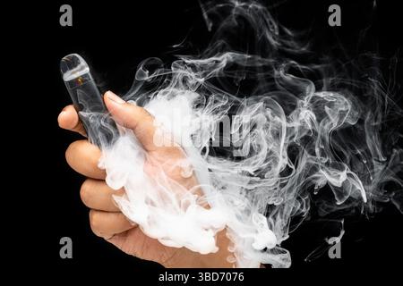 Man vaping and releasing a cloud of vapor with a black background. Vape or electronic cigarette. Modern smoking. No or quit smoking, a bad habit, and Stock Photo