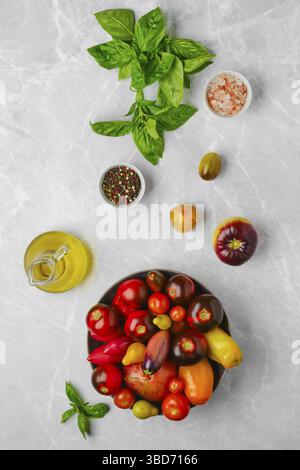 Vertical composition with various types of tomatoes, basil and spice on marble background Stock Photo