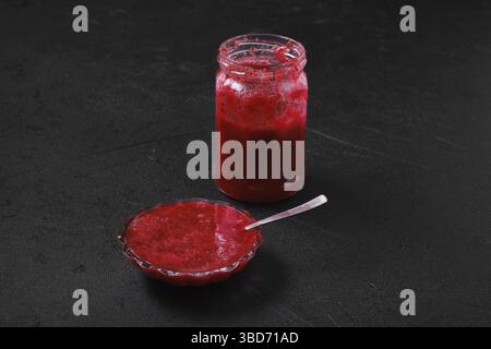 Jar and saucer with cherry jam on black background Stock Photo