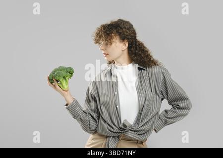 Woman with long curly hair holds broccoli in hand and looking at it Stock Photo