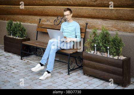 Middle aged man makes online order using laptop outdoors Stock Photo