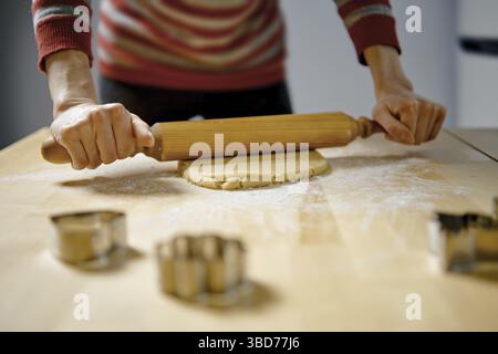 Unrecognizable woman rolls out ginger dough with rolling pin on kitchen table (low angle view with selective focus photo) Stock Photo