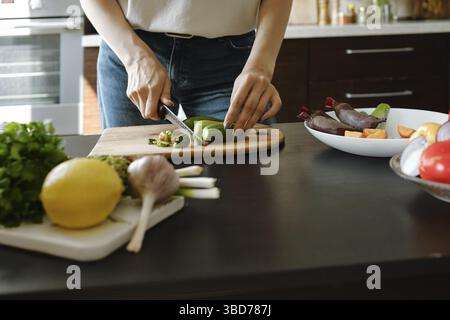 Close-up of female hands chopping fresh baby zucchini on wooden board Stock Photo