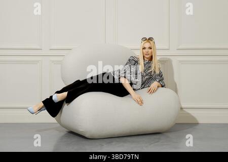 An attractive, stylish woman poses confidently in fashionable clothes and sunglasses while lounging comfortably on a cozy bean bag chair Stock Photo