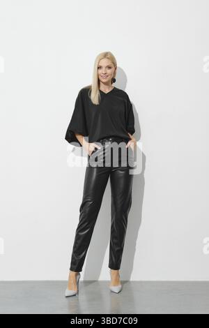 Pretty smiling blonde woman in black blouse and leather trousers Stock Photo