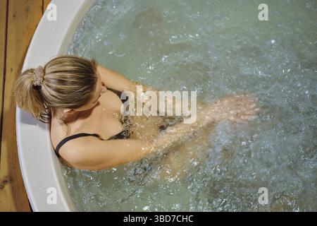 Overhead view of a woman sitting in hot tub with arms fold on her knees Stock Photo