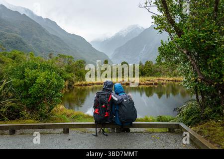 Couple sitting by the Peter’s Pool in the rain, enjoying the views of Franz Josef Glacier valley. West Coast. South Island. Stock Photo