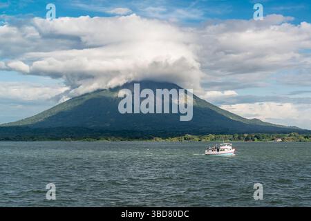 View from Lake Nicaragua on volcano Concepcion with heavy clouds around its top. Passing small white boat in the foreground. Nicaragua. Stock Photo