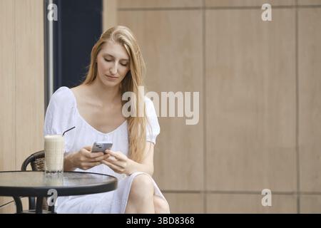 Young woman using smartphone while having coffee break outdoor Stock Photo