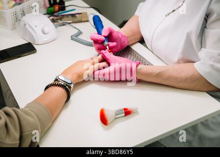 Close-up of a professional performing a manicure using an electric nail file on a client’s hand at a beauty salon. Stock Photo
