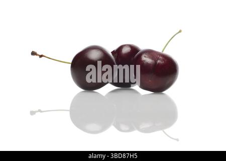 Three fresh cherries with reflection on glossy surface Stock Photo