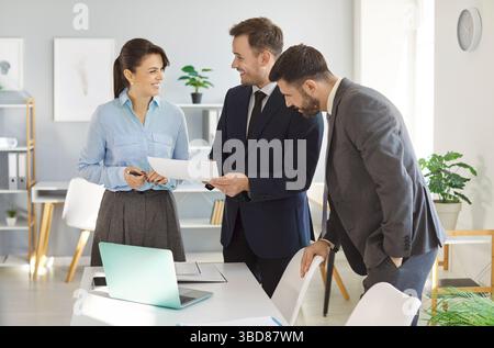 In modern office, three colleagues engage in friendly discussion while reviewing documents. Stock Photo