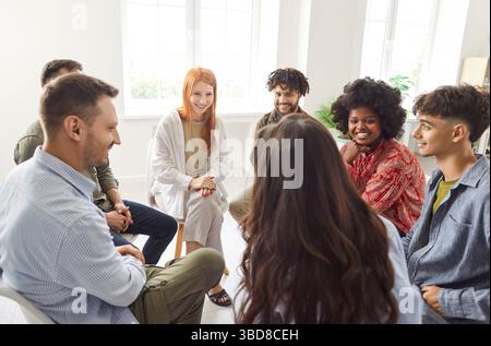 Group of diverse friends, students, colleagues sitting in circle, discussing and laughing together. Stock Photo