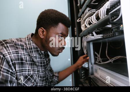 Technician organizes network cables in server rack during evening hours at tech facility Stock Photo
