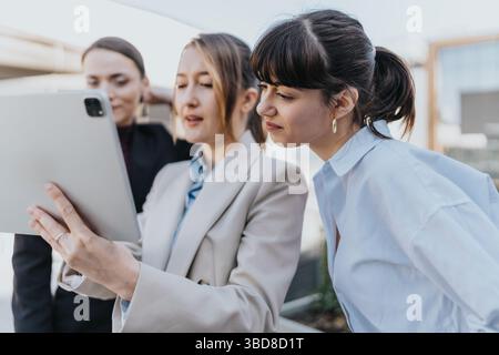 Three female professionals collaborating outdoors using a digital tablet Stock Photo