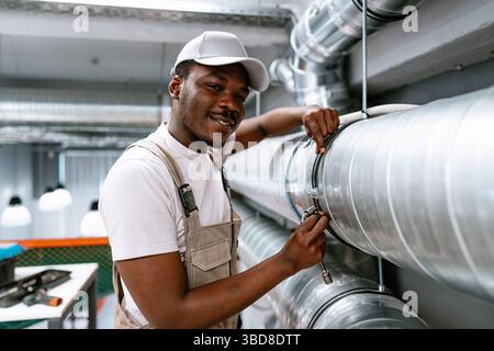 Skilled worker performs maintenance on industrial piping in a modern facility during daytime Stock Photo