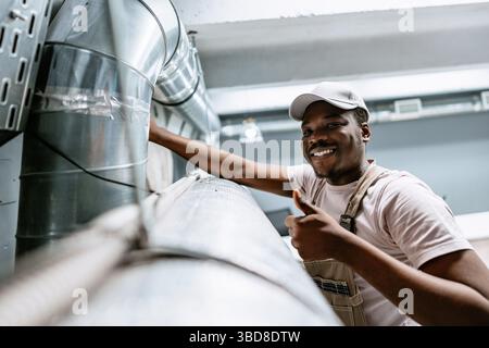 Skilled worker performs maintenance on ventilation system in industrial space during daylight hours Stock Photo
