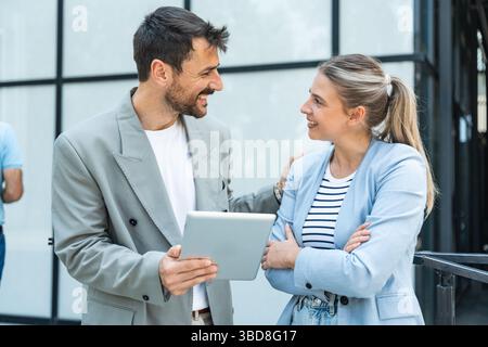 Diverse team of corporate professionals in formal attire collaborating outdoors, engaged in strategic discussion while analyzing data on laptop in fro Stock Photo