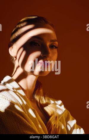 Young beautiful woman poses gracefully, shadow patterns enhancing her captivating features. Stock Photo