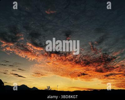Dramatic cloudscape spreading across sunset-lit hills of Abruzzo, Pescara province, illuminating landscape with fiery orange and crimson tones Stock Photo
